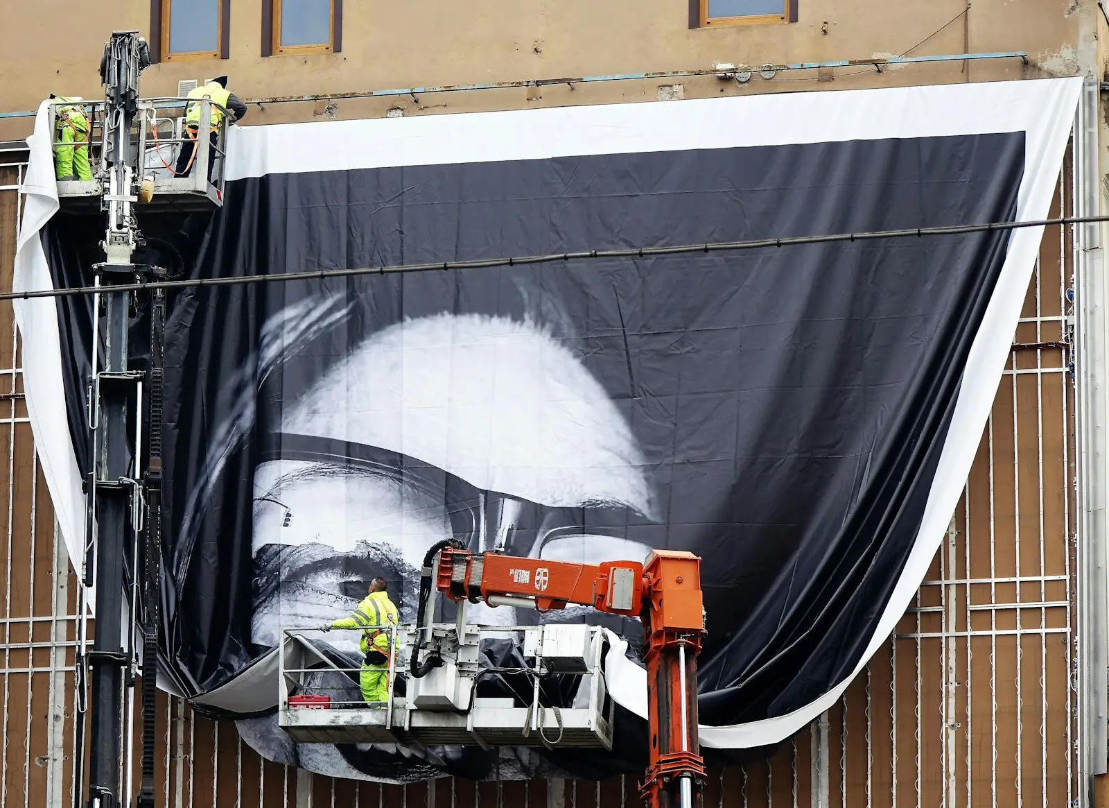 A crew on a boom lift fixing a large-format print to a building