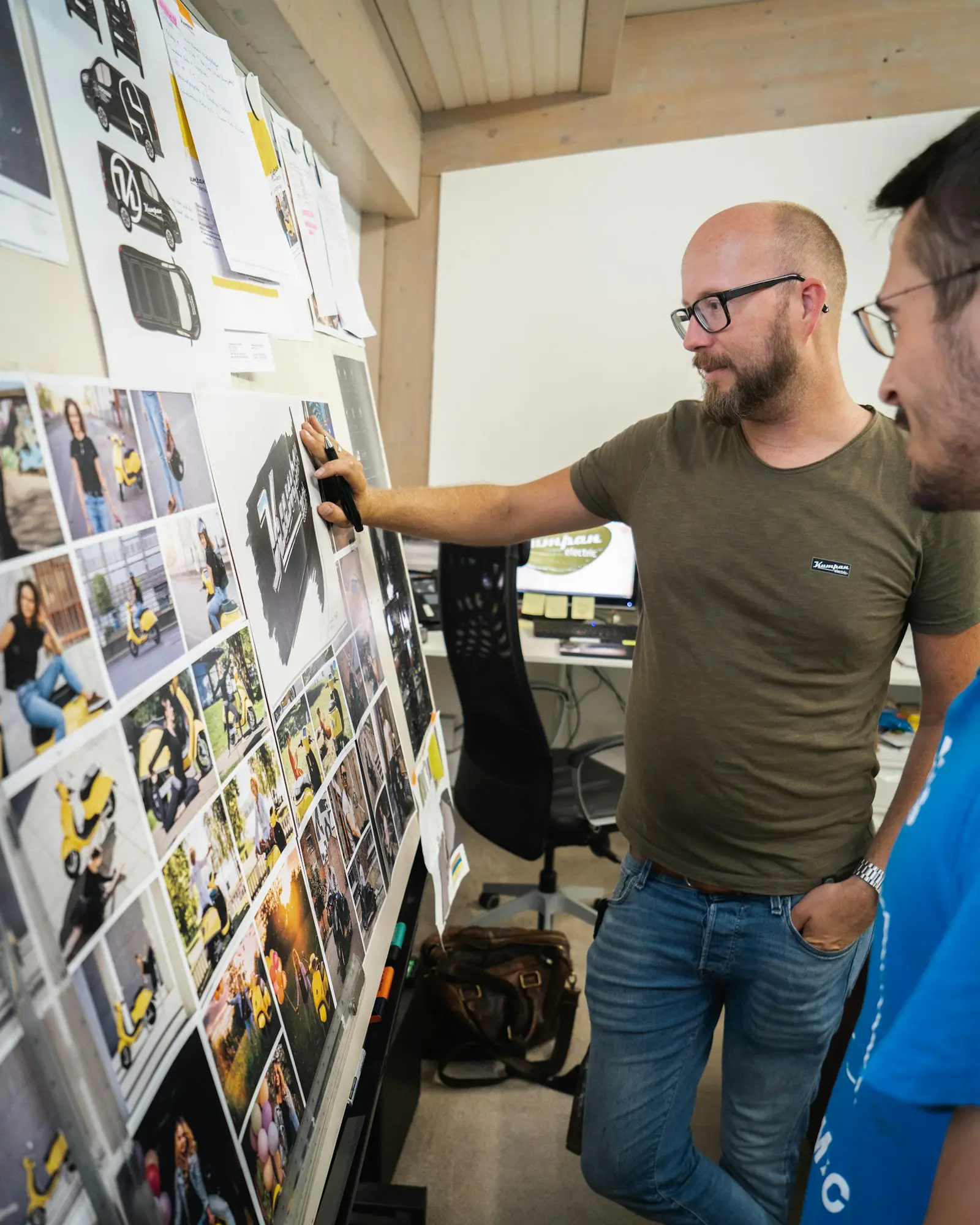 Two colleagues planning a campaign in front of a wall of printed layouts